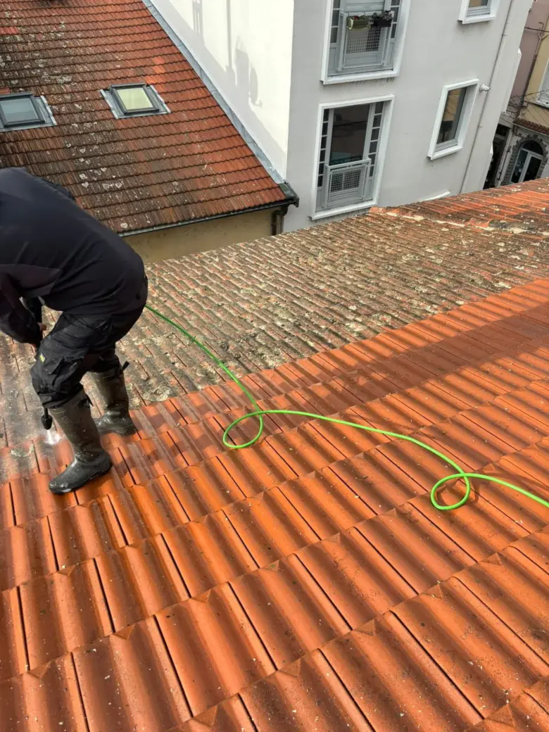 Couvreur zingueur nettoyant une toiture en tuiles au jet basse pression