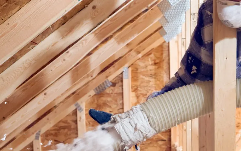 Machine à souffler projetant l'isolant en flocons sur le plancher des combles