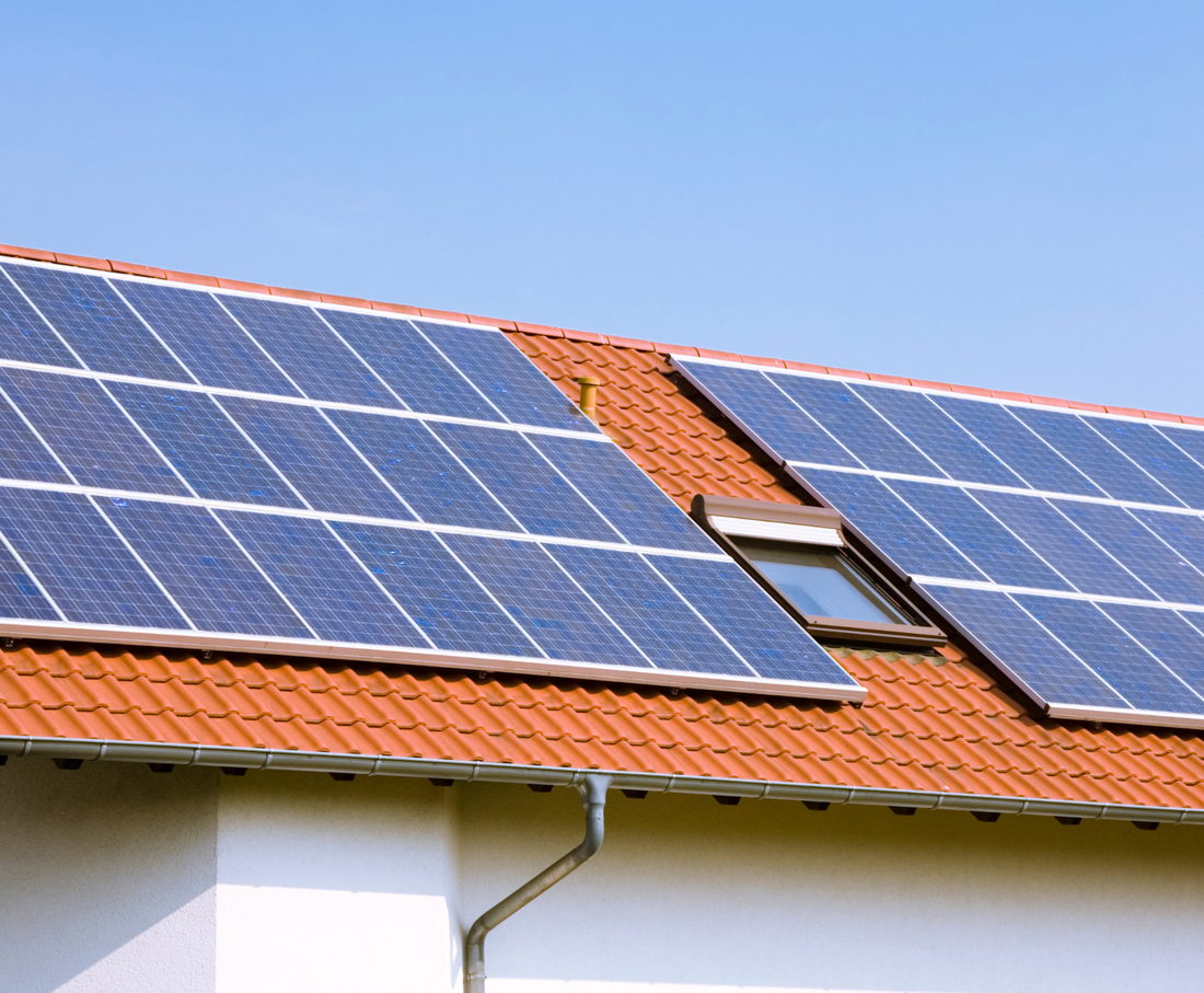 Panneaux solaires posés sur une toiture en tuiles, à côté d'une fenêtre de toit