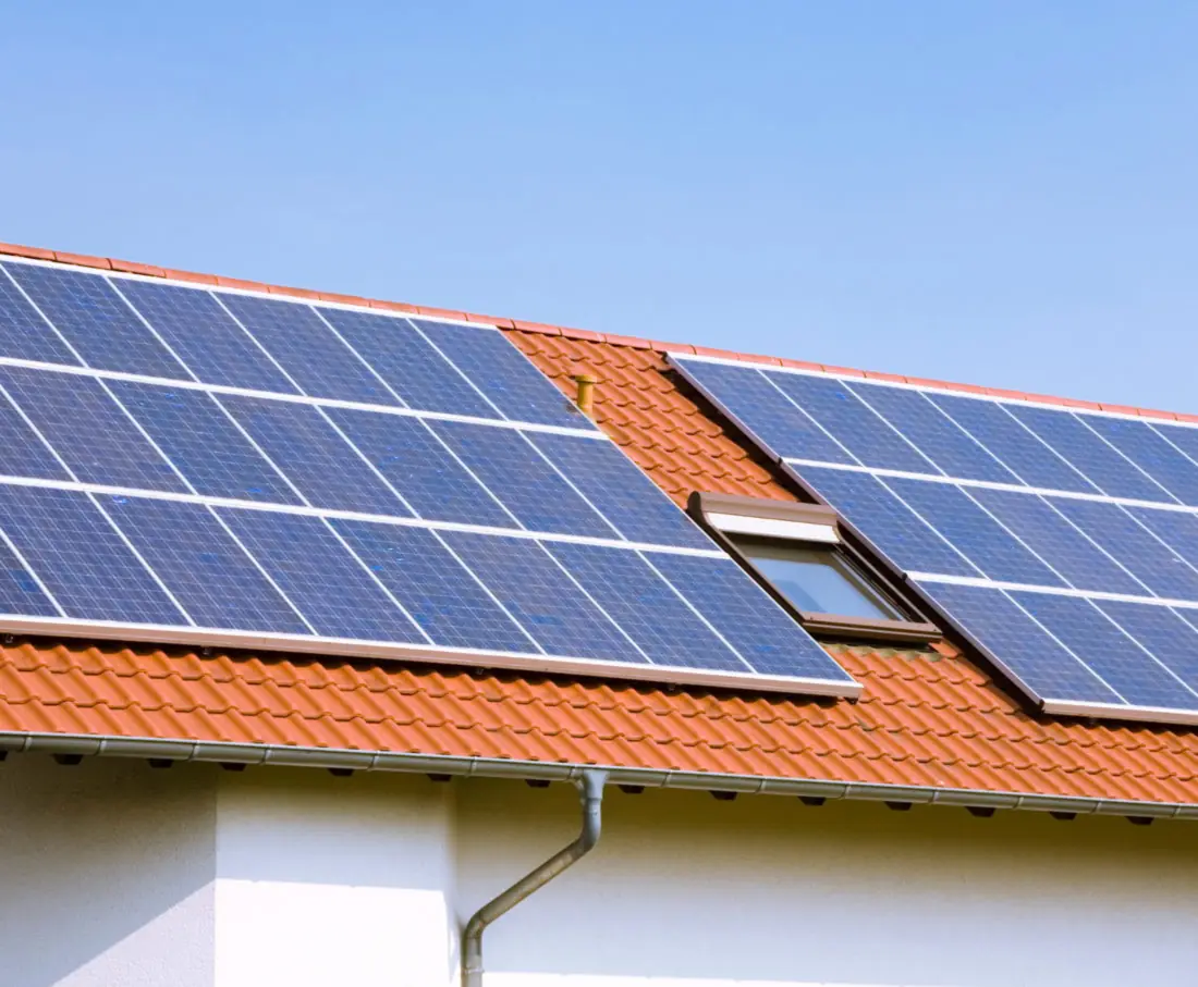 Panneaux solaires posés sur une toiture en tuiles, à côté d'une fenêtre de toit