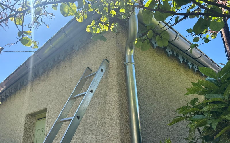 Descente d'eau pluviale neuve fixée le long d'un mur crépi