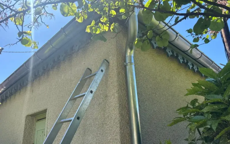 Descente d'eau pluviale neuve fixée le long d'un mur crépi