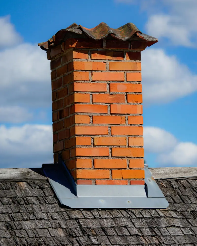 Souche de cheminée en briques neuves coiffée d'un chapeau, sur une couverture en ardoises
