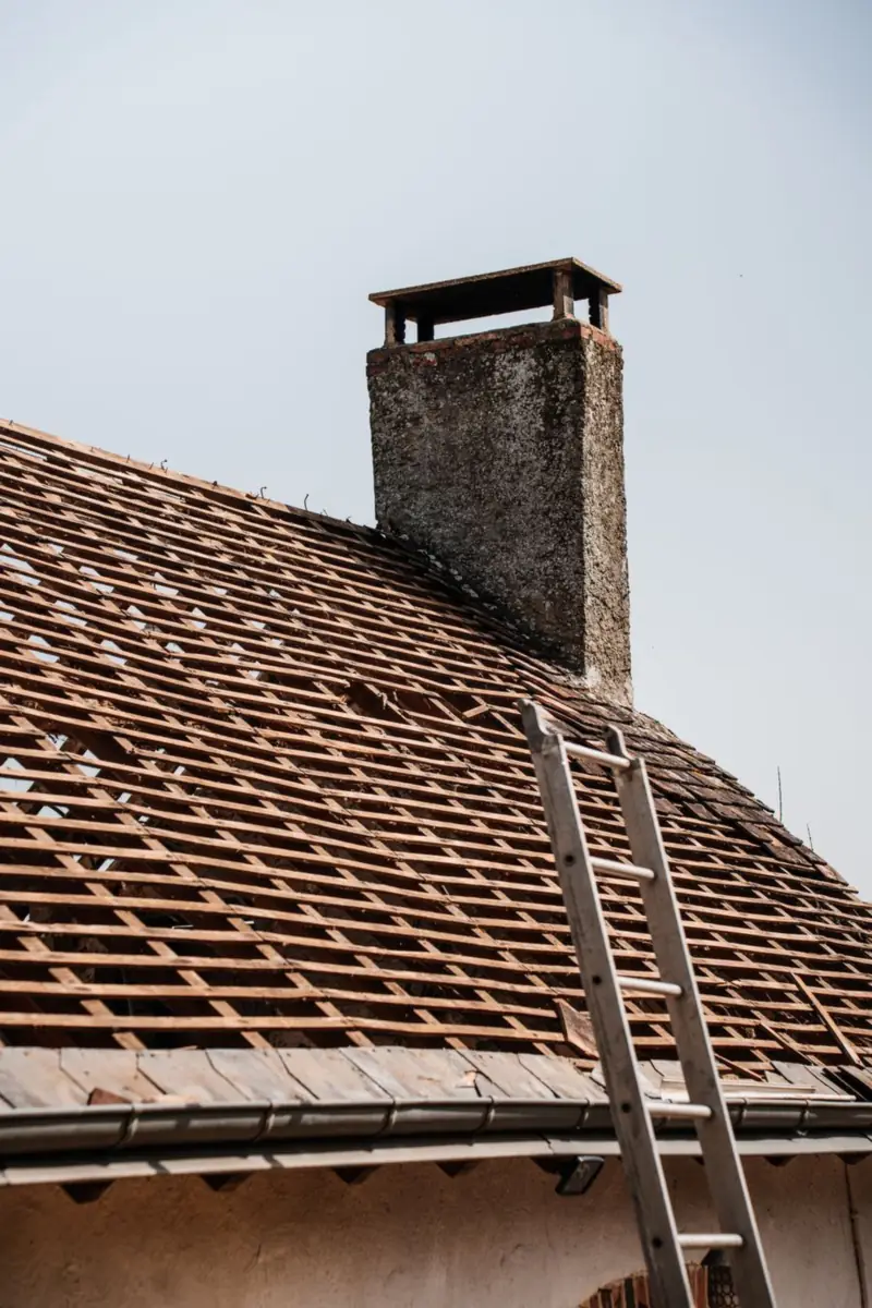 Maison ancienne en cours de rénovation de toiture, échelle de couvreur appuyée sur la façade