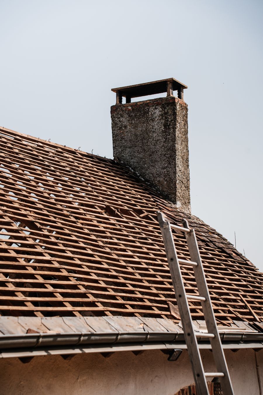 Maison ancienne en cours de rénovation de toiture, échelle de couvreur appuyée sur la façade